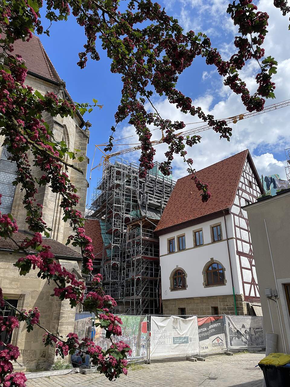 Außenansicht der Rückseite des historischen Rathauses in Forchheim mit der teilrestaurierten Fassade. Im Bild noch ein Teil der Kirche St. MArtin sowie einige blühende Äste des Rotdorns.