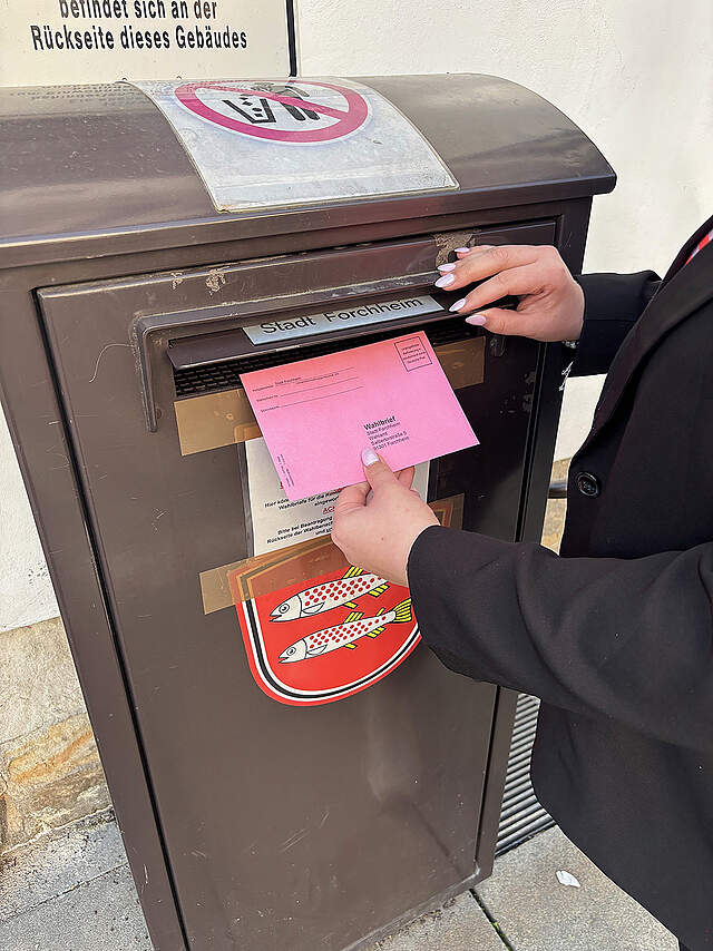 Eine Person wirft einen Wahlbrief in einen Briefkasten.