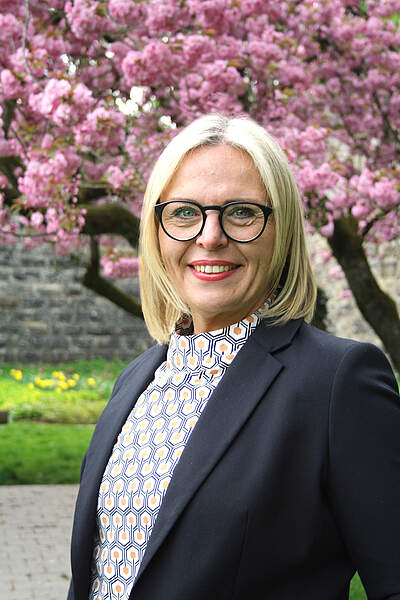 Portraitaufnahme von Oberbürgermeisterin Martina Hebendanz im Stadtpark. Im Hintergrund eine blühende Zierkirsche.