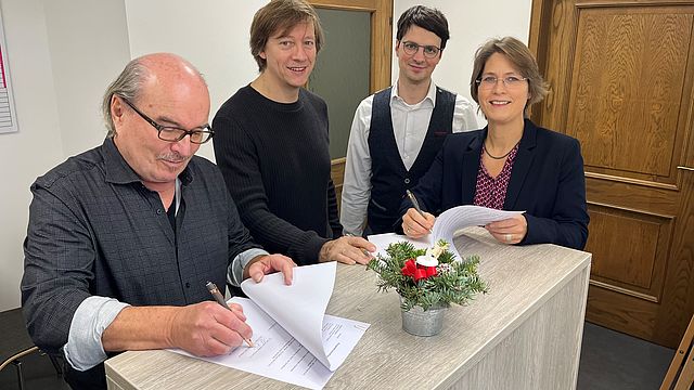 Drei Männer und eine Frau unterzeichnen in einem Büro einen Vertrag.