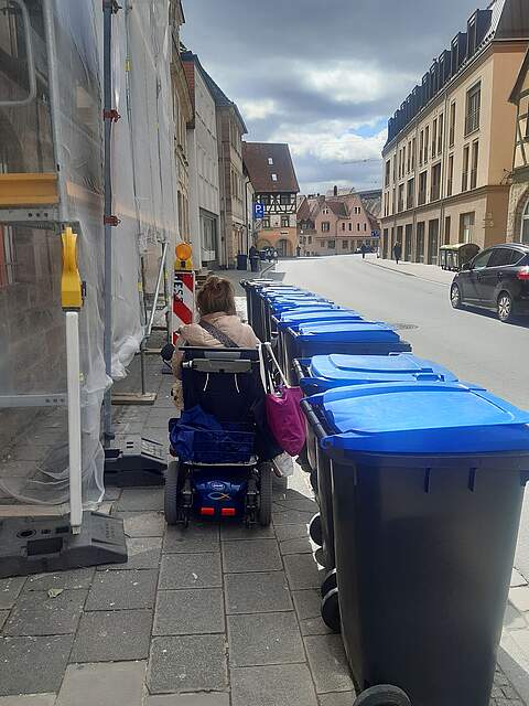 Mülltonnen am Straßenrand, Rollstuhlfahrerin versucht hindurch zu kommen.