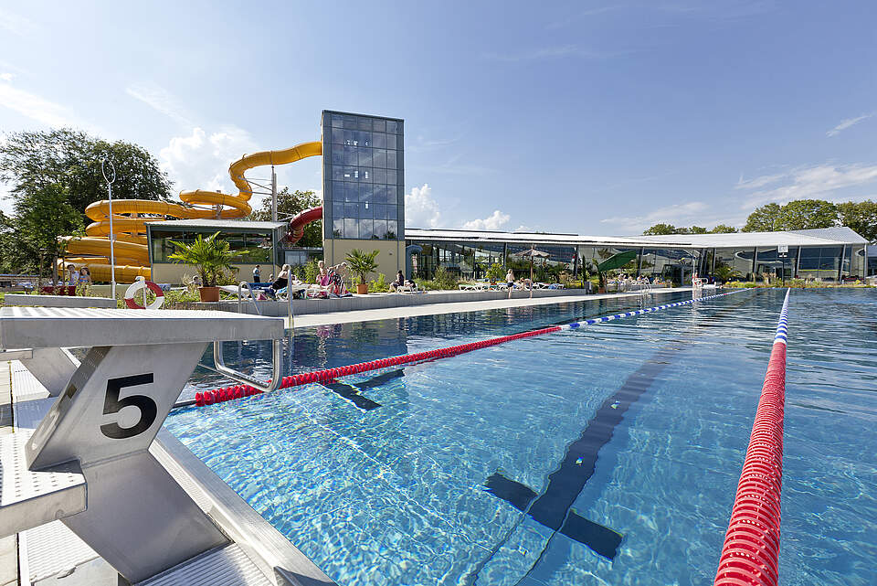 Außenbecken Königsbad Forchheim Außensportbecken mit rot-weißen Bahnabtrennungen undim Hintergrund das Hallenbad mit angrenzendem Rutschenturm.rgrund befindet sich ein Startblock.