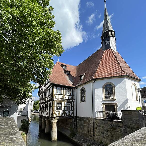 Spitalkirche mit Fachwerkbau auf Pfählen, die in einen Fluss reichen.