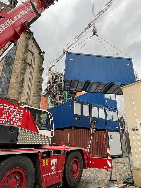 Ein Kran stapelt große Baucontainer übereinander.