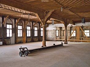 Ein großer Saal mit vielen Fenstern und einer aufwändig gestalteten historischen Holzdecke ist zu sehen.