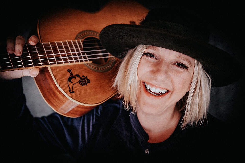 Künstlerin mit Hut und Gitarre auf der Schulter