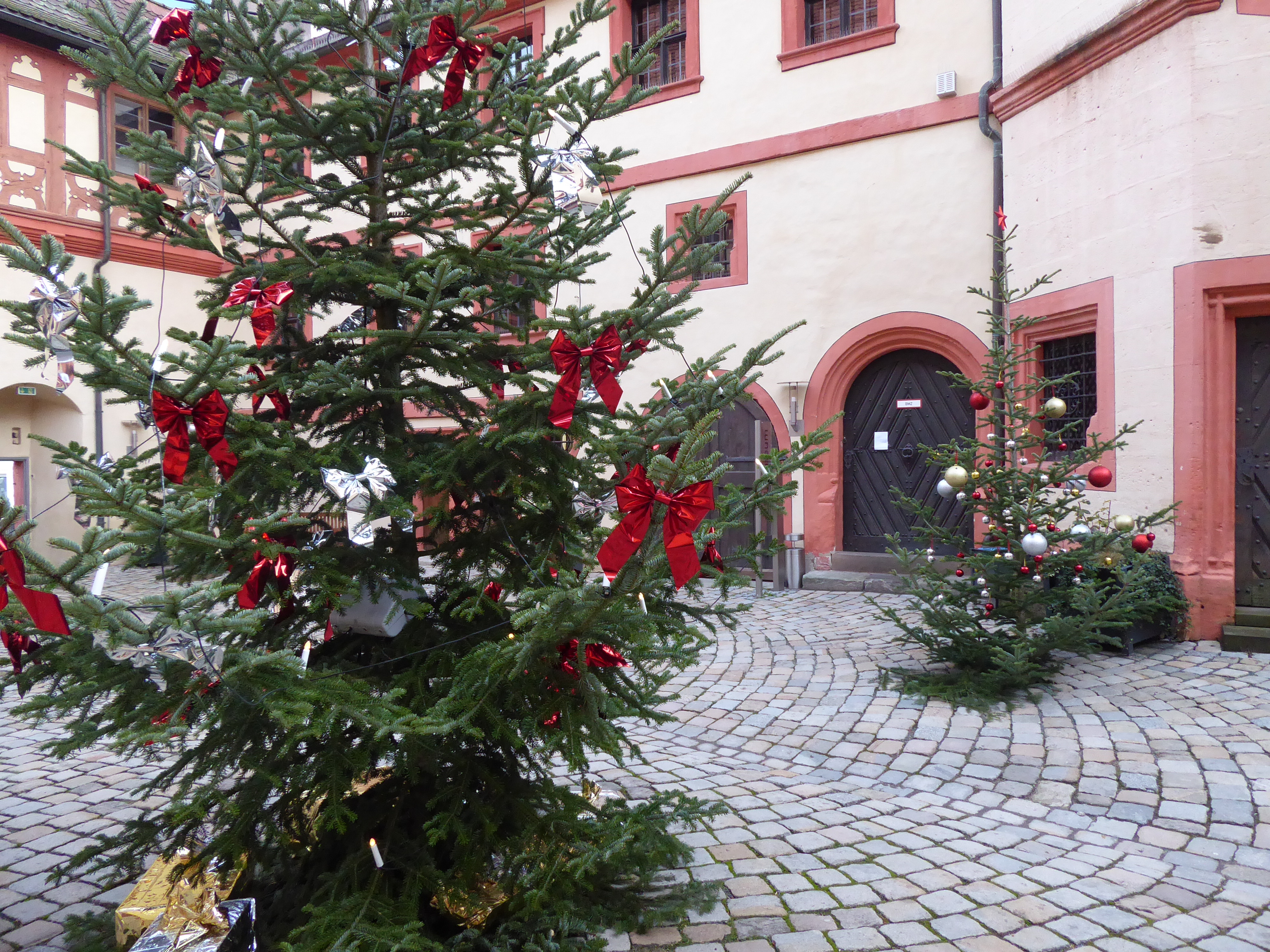 Innenhof eines historischen Schlosses mit weihnachtlich geschmückten Christbäumen.
