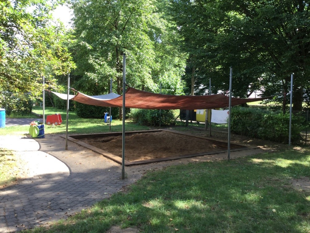 Außenspielbereich mit überdachtem Sandkasten und Schaukeltieren.