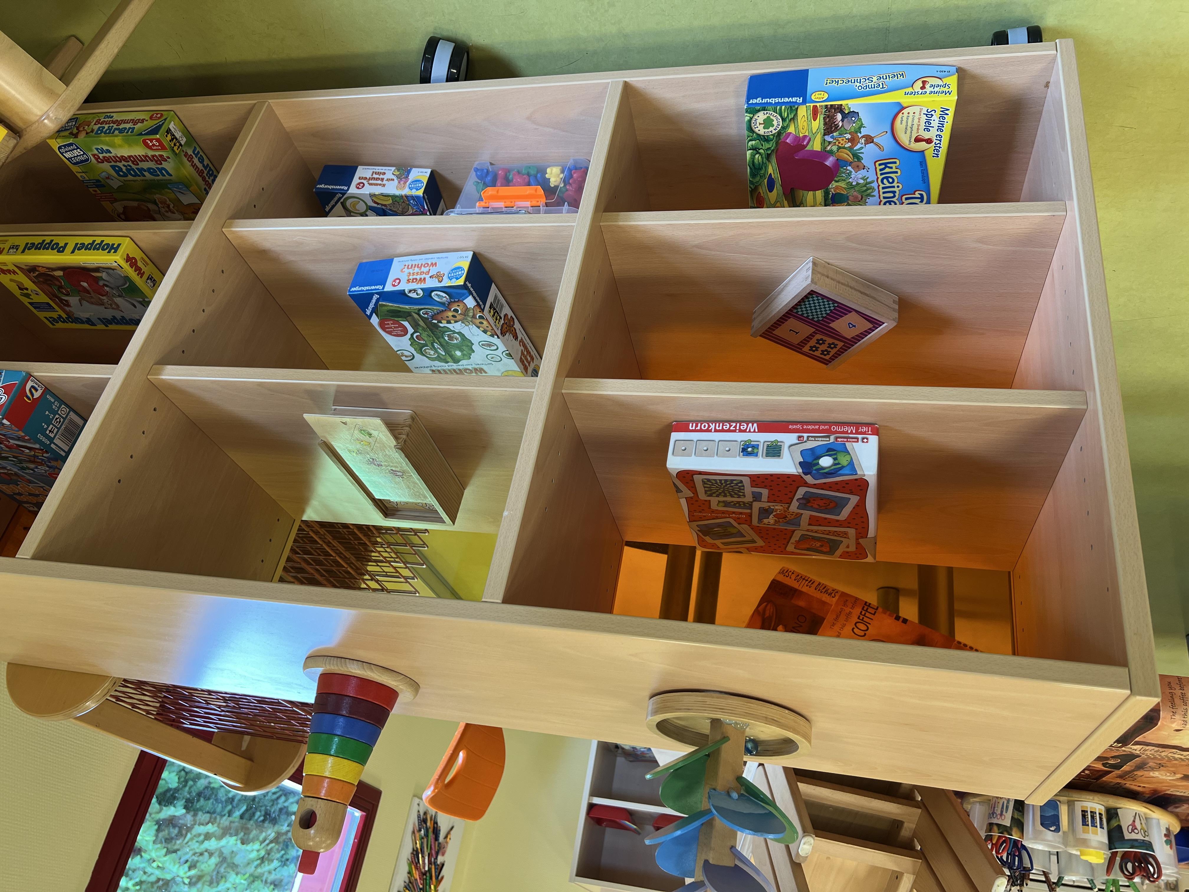 In einem Regal in einem Kindergartengruppenraum stehen verschiedene Kinderspiele zur Auswahl bereit.