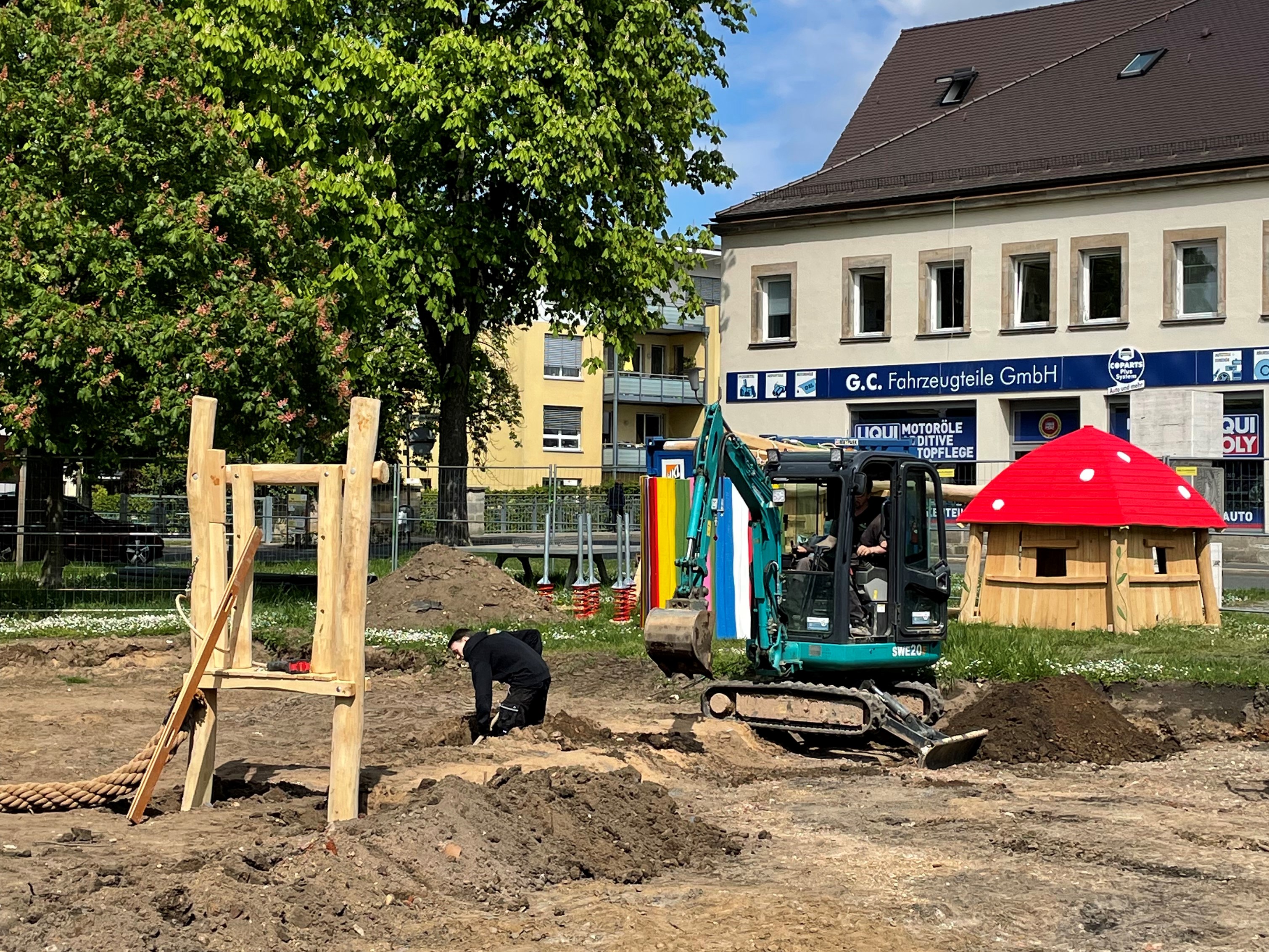Ein Holzspielhaus mit buntem Dach, Kletter- und Balanciergeräte werden auf einem Spielplatz aufgebaut.